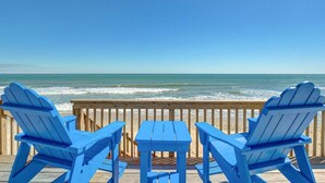 A wooden deck with three blue Adirondack chairs and a small table, overlooking a beach with waves. - Stunning beachfront home with ocean-view decks and direct beach access in Surf City (Surf City)