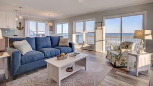 A spacious living room with a blue sofa, a white coffee table, and a view of the ocean through large windows. - Stunning beachfront home with ocean-view decks and direct beach access in Surf City (Surf City)