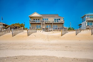 A beachfront property with a two-story building, a wooden fence, and a sandy beach. - Spacious Oceanfront Retreat with Private Beach Access, Elevator, Game Room & Incredible Views (Surf City)