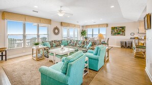 A spacious living room with a large sofa, two armchairs, a coffee table, and a dining area.