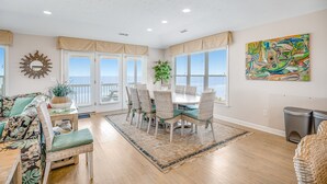 A dining area with a table and chairs, a sofa, a potted plant, and a view of the ocean.
