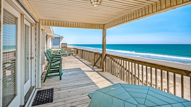 A wooden deck with a view of the ocean, outdoor seating, and a covered area with a table and chairs.