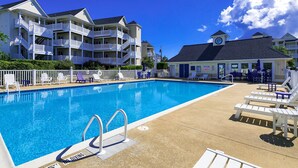 A pool area with a clear blue pool, white lounge chairs, and a building with multiple balconies. - Waterfront Condo w/ Free WiFi, Central AC, Private Washer/Dryer, Shared Pool (Hatteras)
