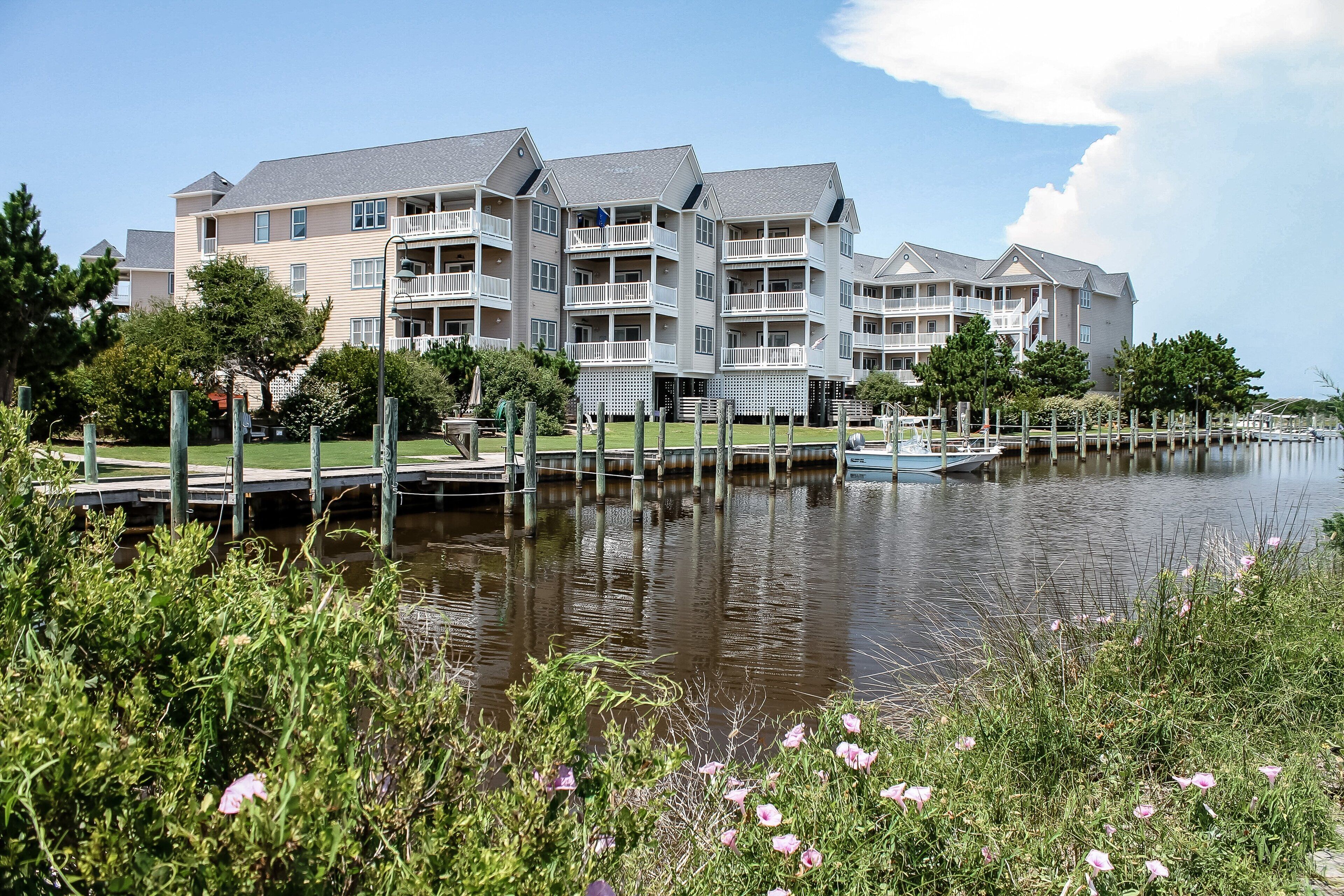 A multi-story residential building with balconies, a dock, and a calm water body in front.