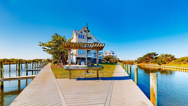 A wooden pier leading to a house with a gazebo, a clear blue sky, and water on both sides. - Waterfront Condo w/ Free WiFi, Central AC, Private Washer/Dryer, Shared Pool (Hatteras)