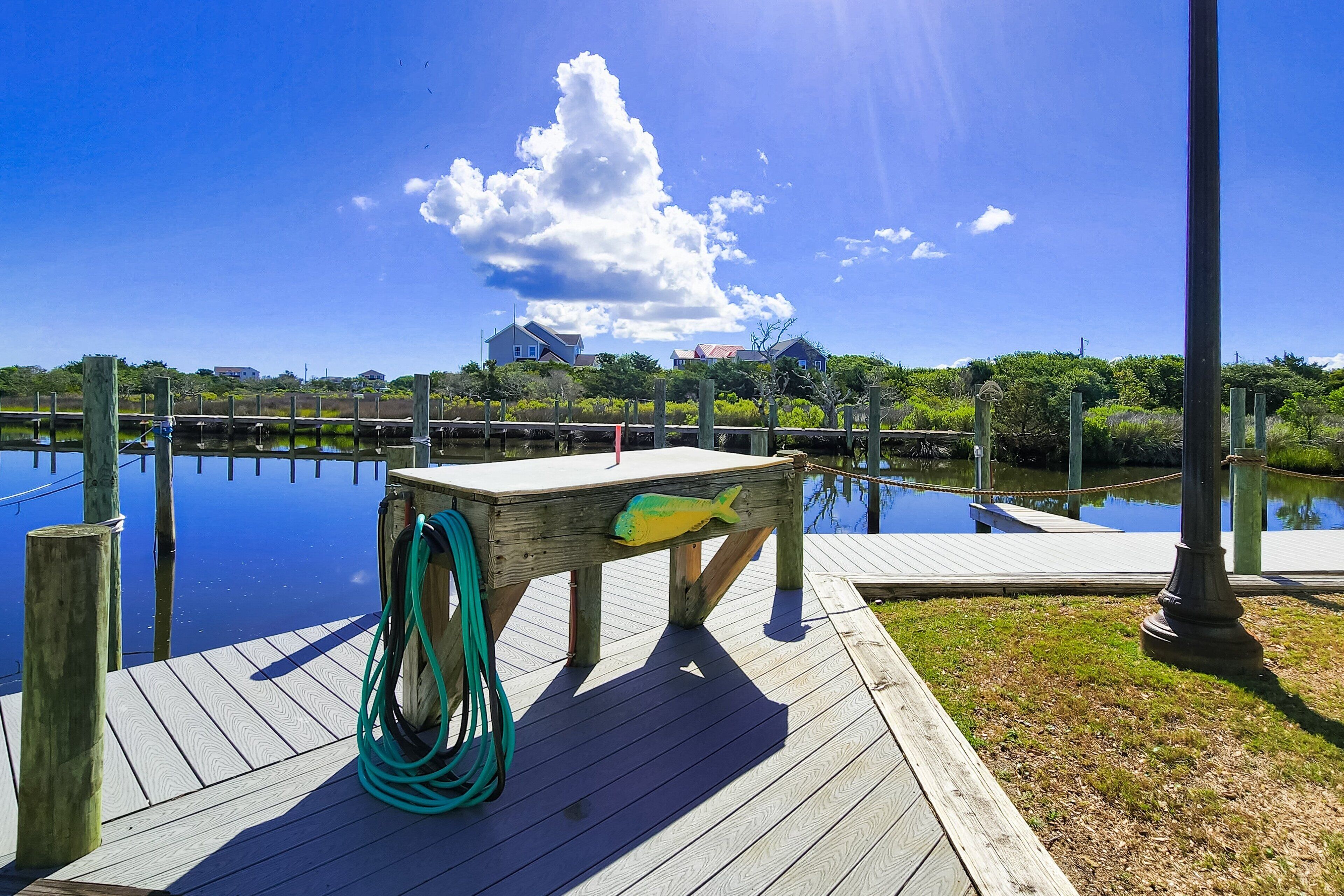 A wooden dock with a green hose, a fish sculpture, and a clear view of the water and sky.