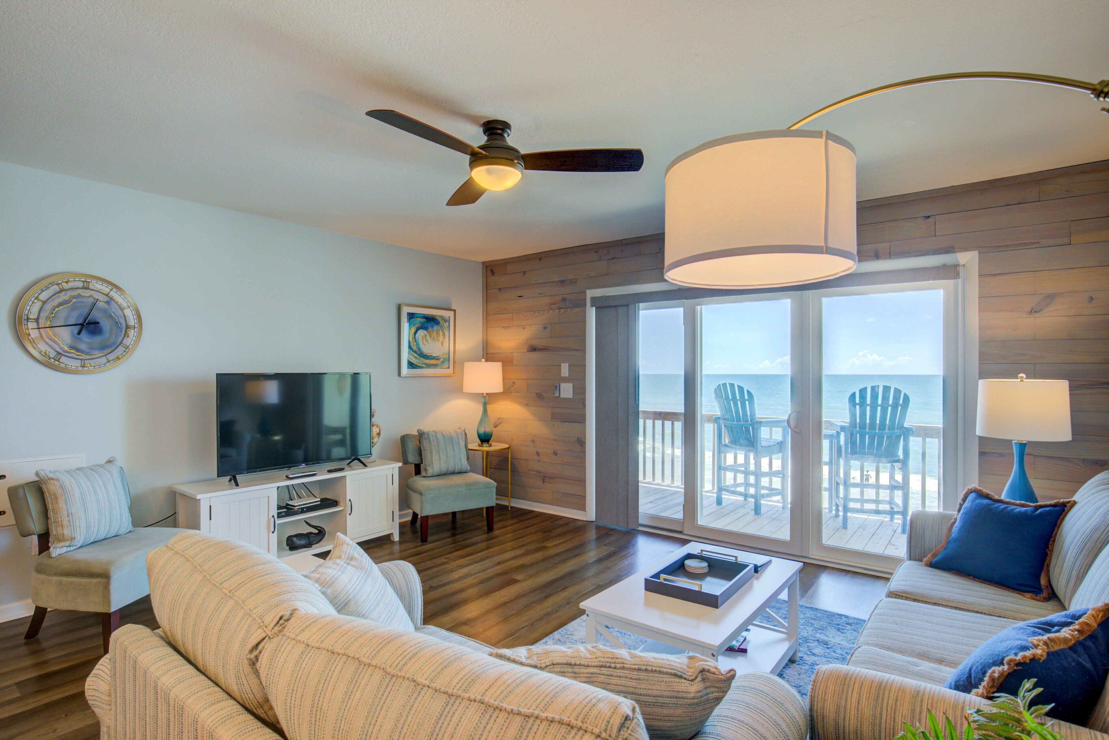 A living room with a television, seating, a ceiling fan, and a view to the outside.