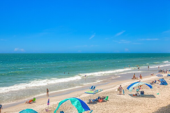 A beach with clear skies, people swimming and relaxing, and beach umbrellas and chairs.