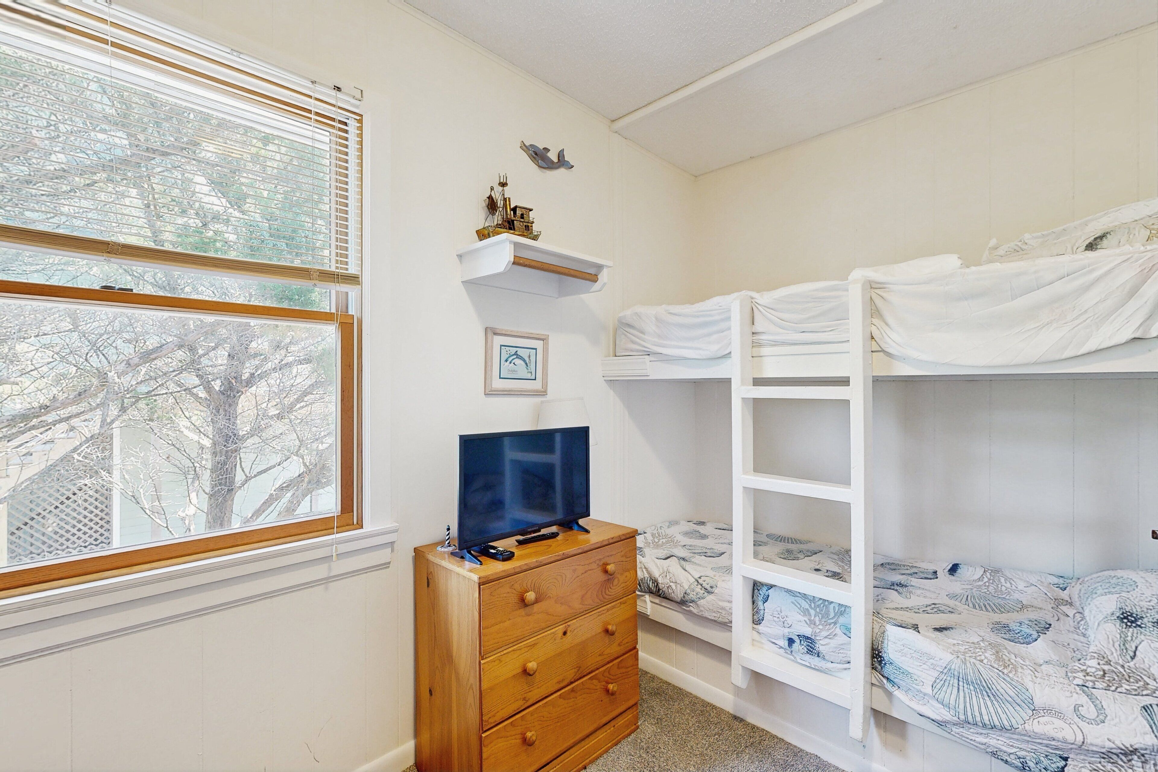 Une chambre avec des lits superposés, une commode, un téléviseur et une fenêtre avec des stores.