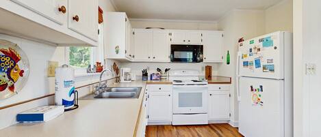 Una cocina con armarios blancos, un microondas, una estufa y un refrigerador.