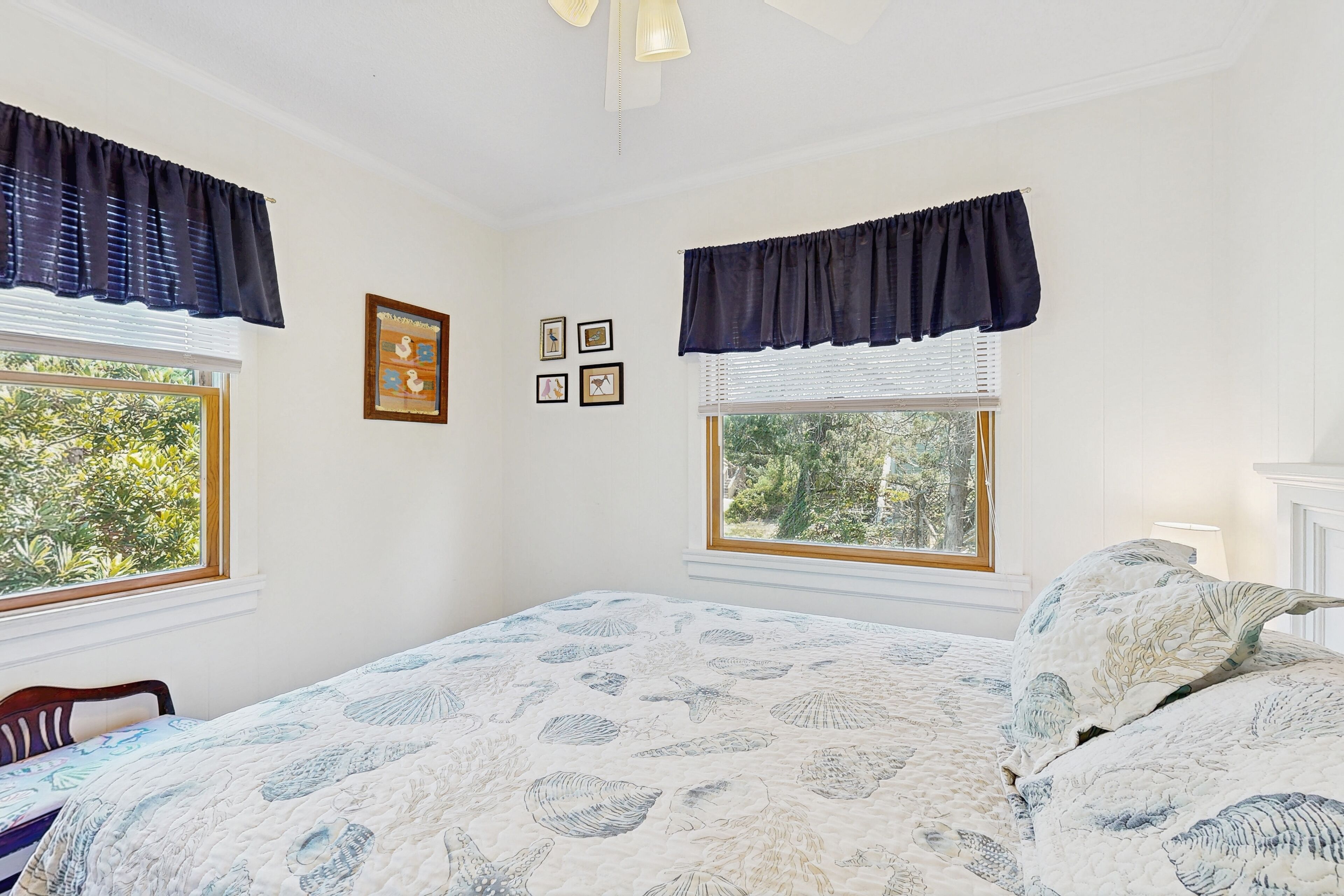 Un dormitorio con una cama grande, dos ventanas con cortinas y un ventilador de techo.