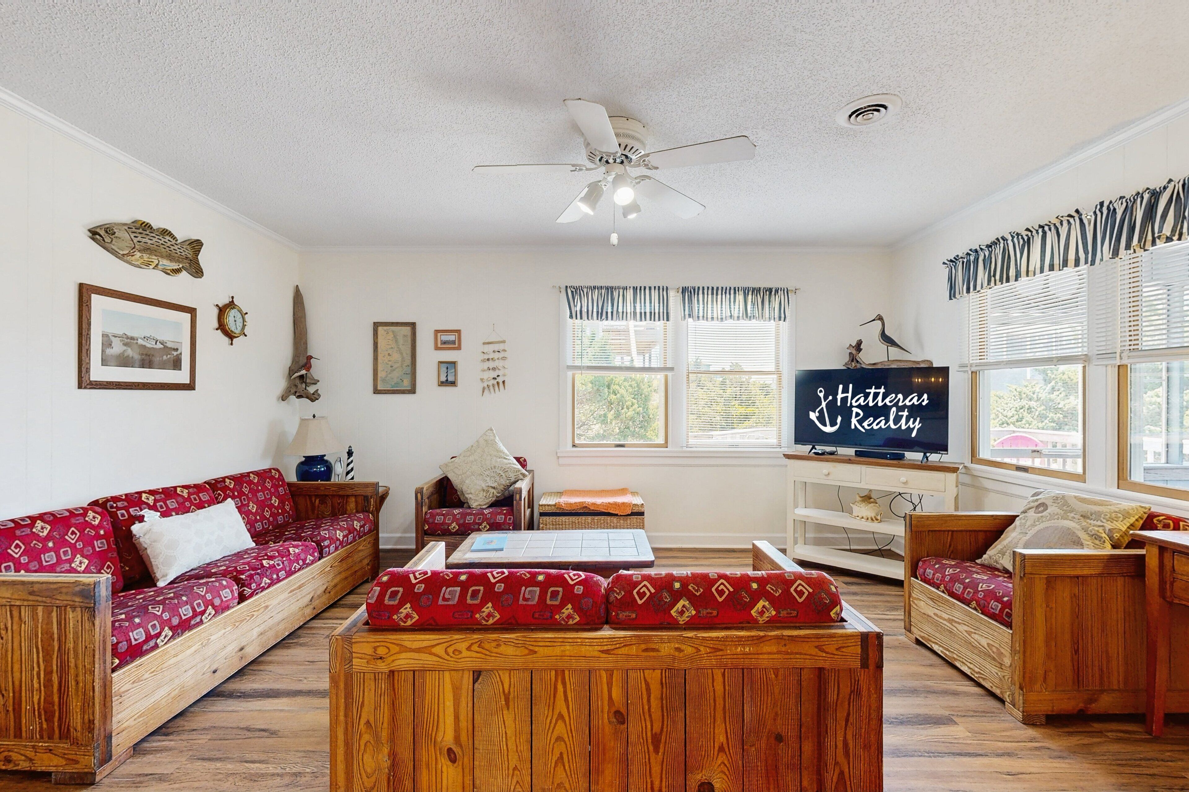 A cozy living room with a red patterned sofa, wooden coffee table, and a television displaying 'Hatteras Realty'.