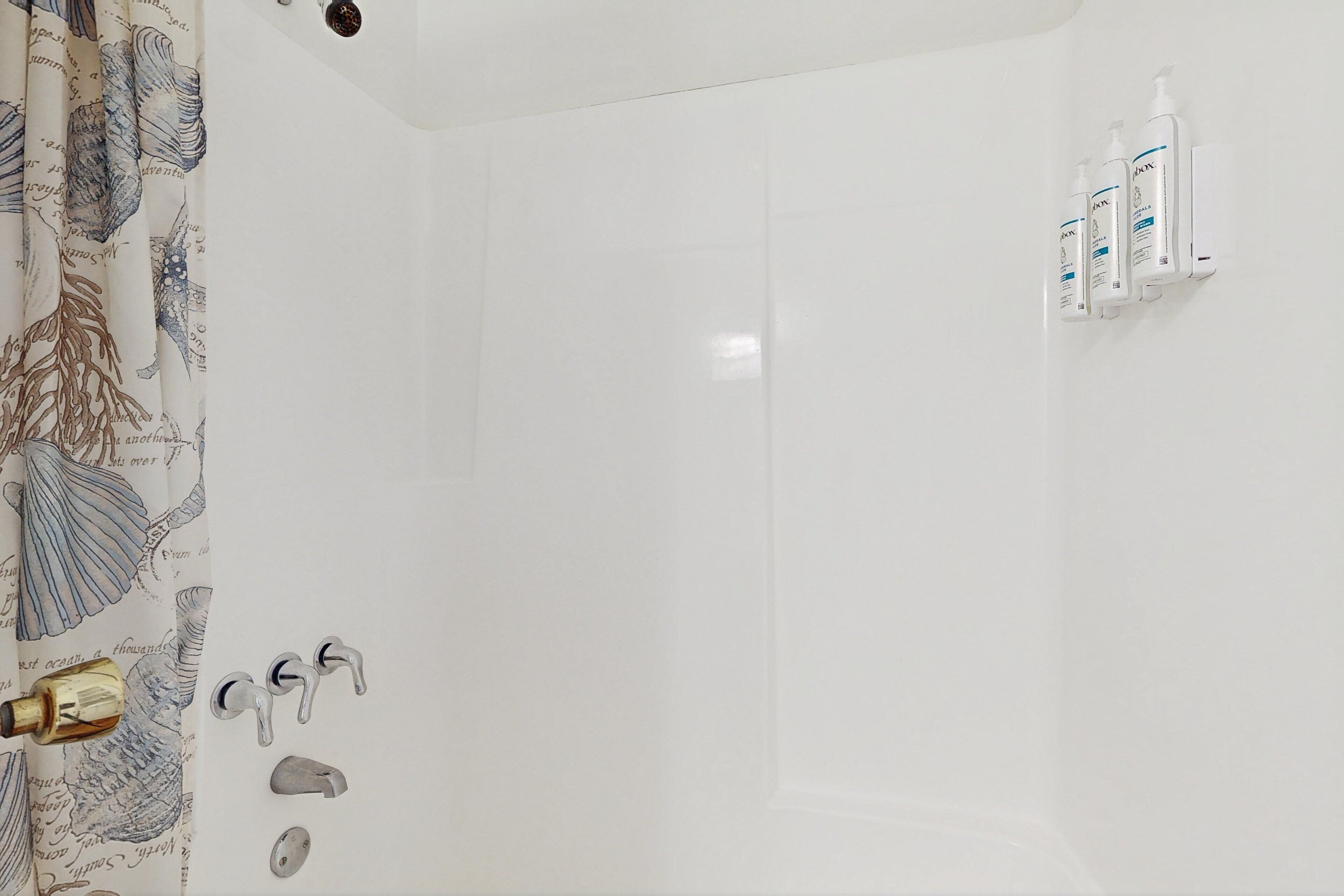 A bathroom with a shower, a toilet, and a sink. There are three bottles of shampoo on the wall.