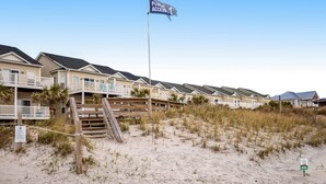 A beachfront hotel with multiple-story buildings, a public access sign, and a sandy beach area. - Beachfront home with beach access, community pool, foosball table, ocean views (Surf City)