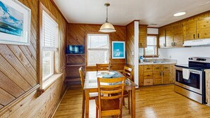 A kitchen with wooden walls, a dining table with chairs, a stove, and a window with blinds. - Tarpon Drive Hideaway B:Dog-friendly duplex w/Balcony (Avon)