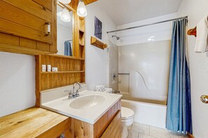 Ein Badezimmer mit Waschtisch aus Holz, einem Waschbecken, einer Toilette und einer Dusche mit Duschvorhang.