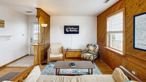 A cozy living room with wooden walls, a sofa, a coffee table with a book, a chair, and a framed picture on the wall. - Tarpon Drive Hideaway B:Dog-friendly duplex w/Balcony (Avon)