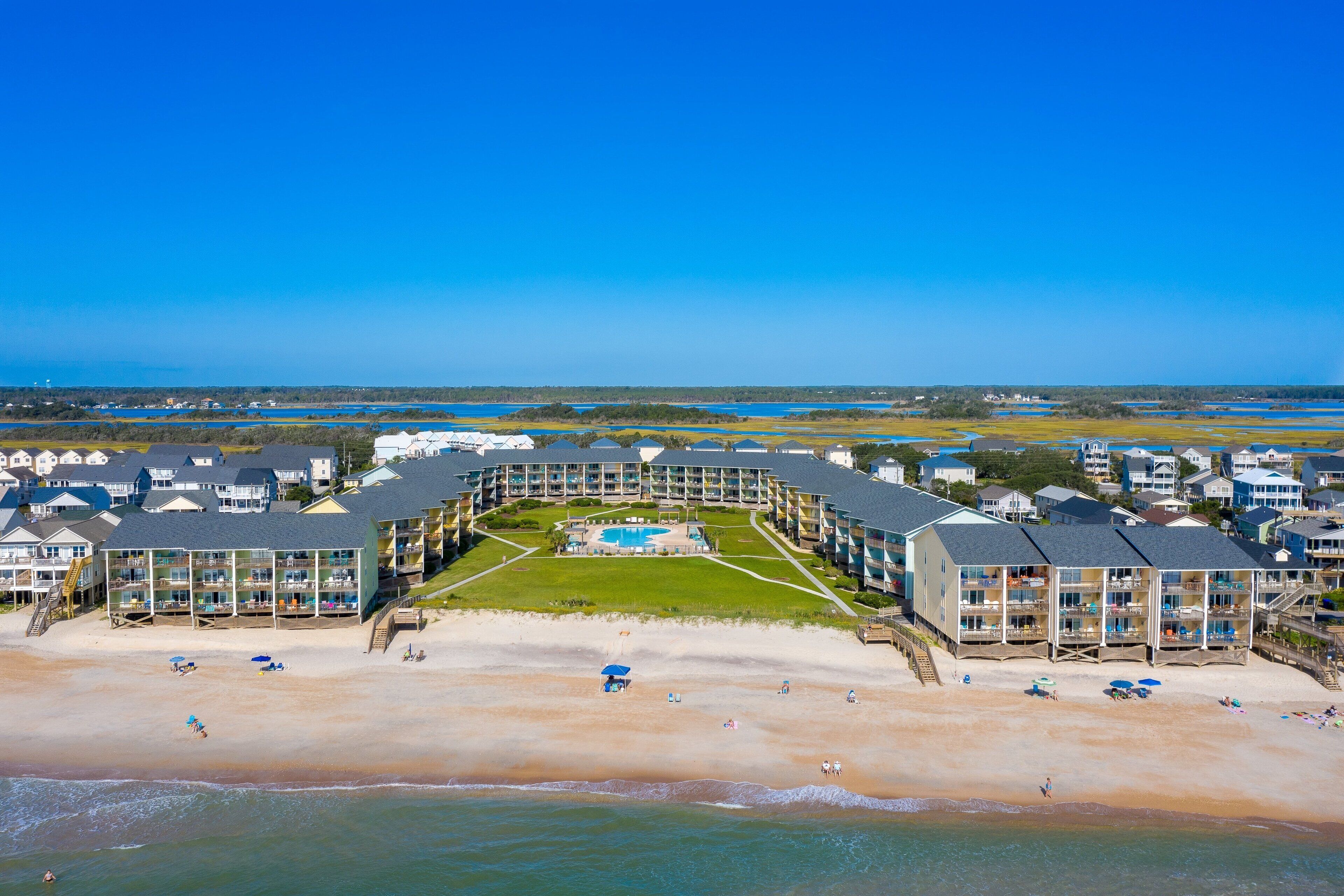 A beachfront hotel with multiple buildings, a swimming pool, and a beach area with umbrellas and sun loungers.