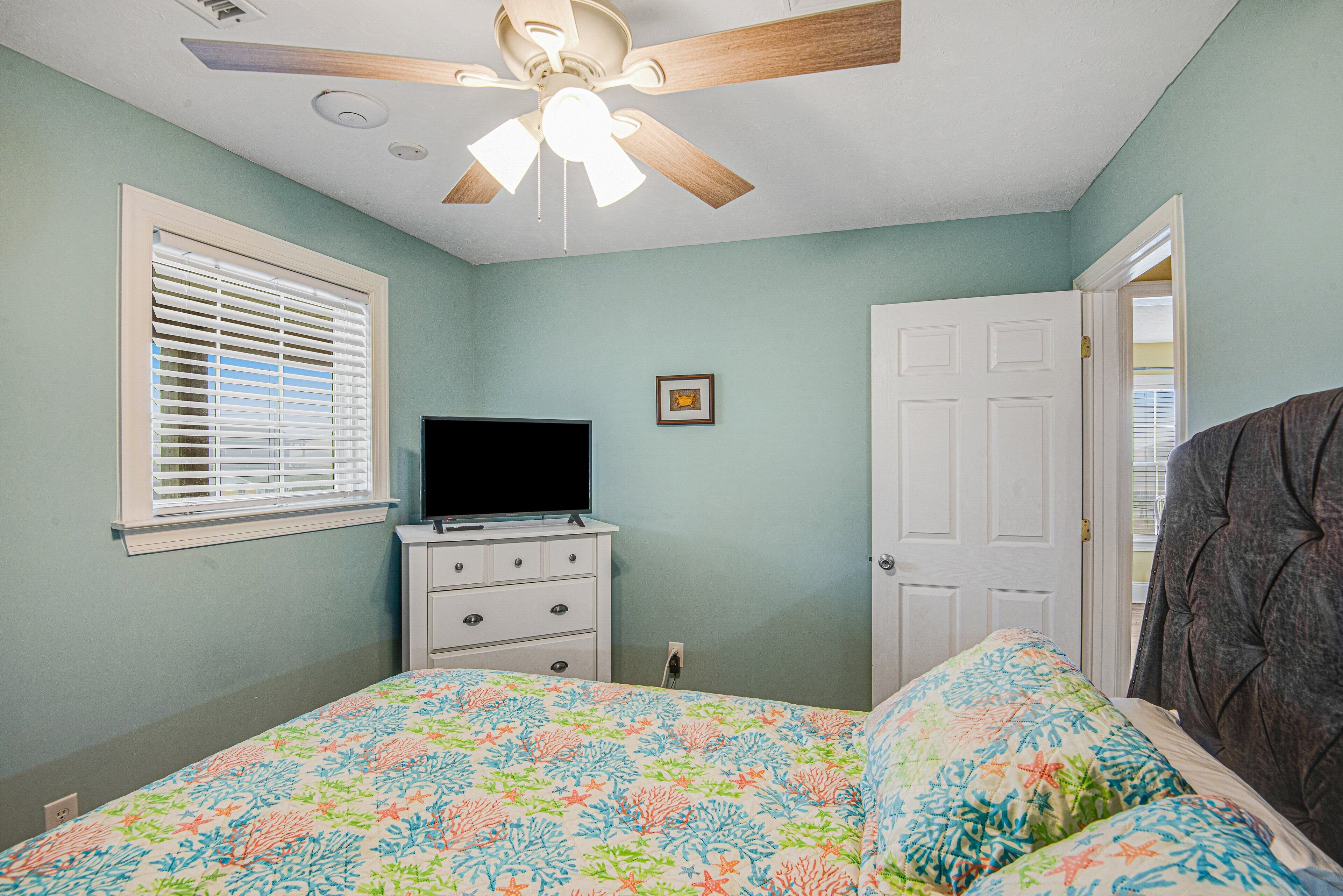 A bedroom with a bed, a dresser, a television, a ceiling fan, and a door.