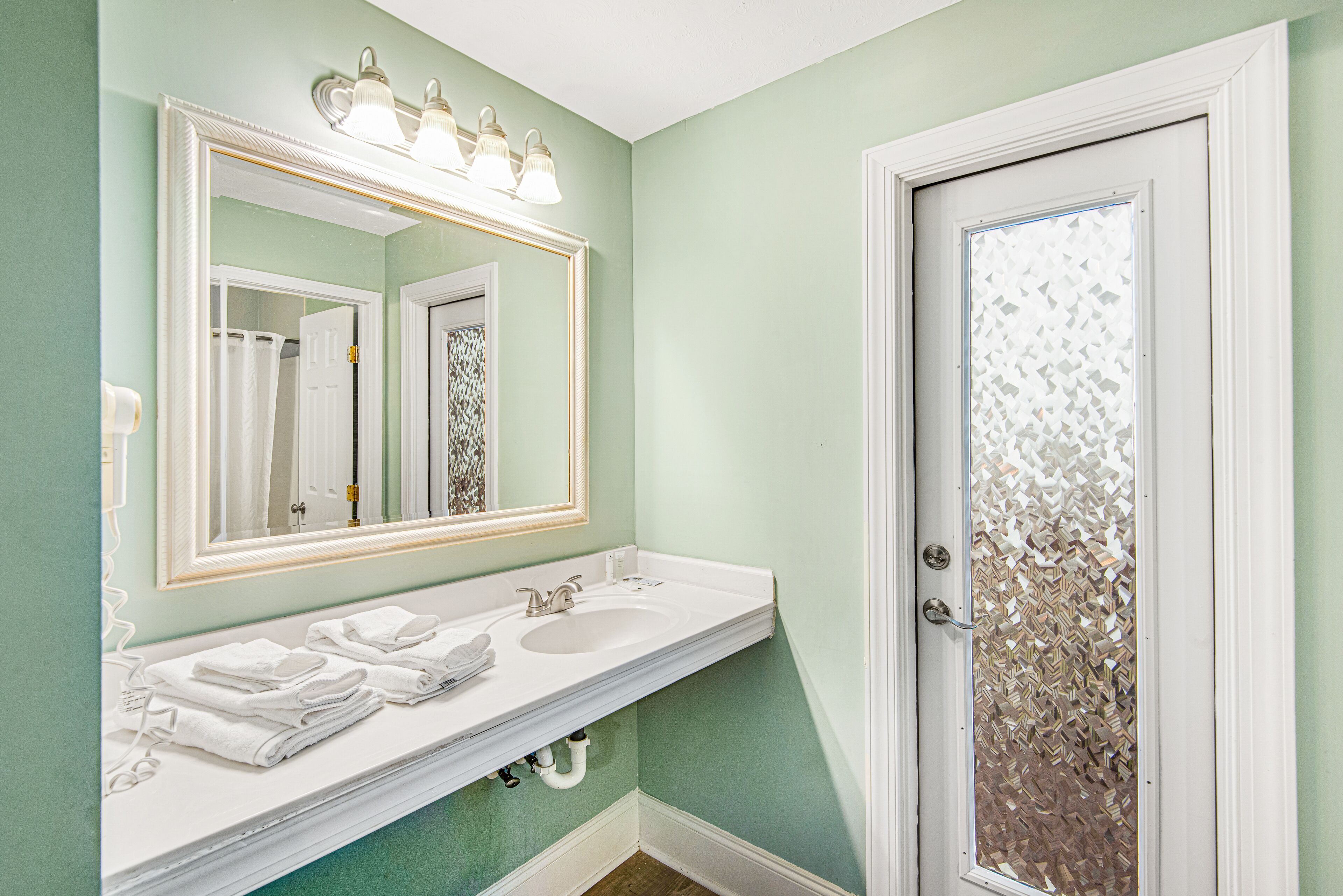 A bathroom with a white vanity, a large mirror, and a frosted glass door.