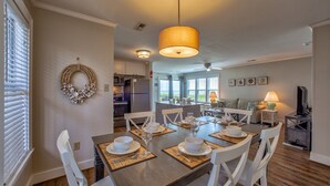 A dining area with a wooden table set for four, white chairs, and a hanging light fixture. - Bright, updated oceanfront home with shared pool, private deck, & great views (Avon)