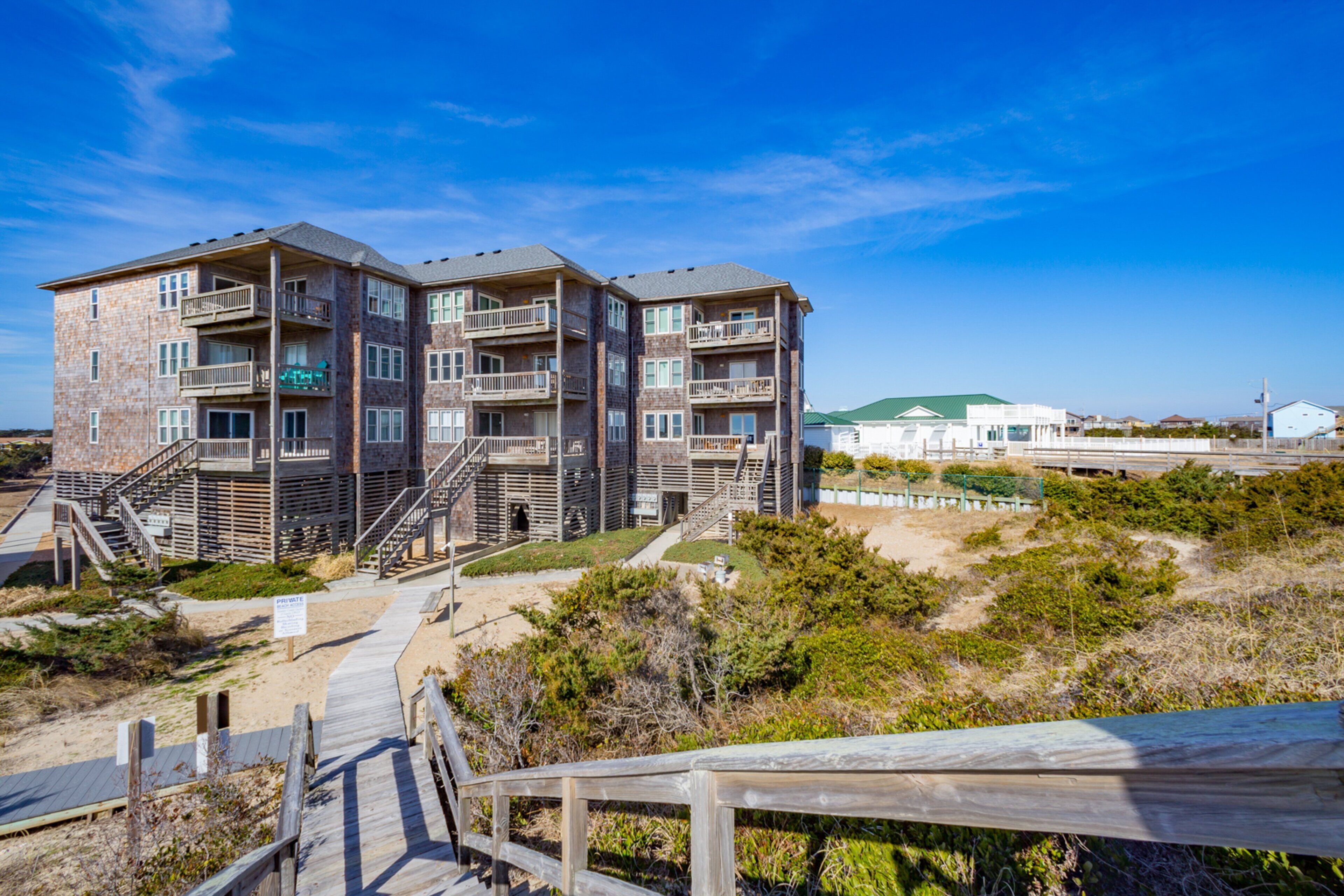 A multi-story building with balconies, a wooden deck, and a sandy area in front.
