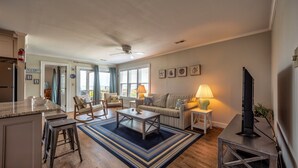 A spacious living room with a large window, a sofa, a coffee table, and a TV stand. - Bright, updated oceanfront home with shared pool, private deck, & great views (Avon)