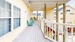 A covered wooden deck with chairs, a railing, and a view of neighboring houses. - Ocean-view townhome with pool access, playground, outdoor shower - dog-friendly (Surf City)