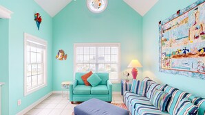A room with teal walls, a teal sofa, a striped sofa, a window with blinds, a ceiling fan, and a wall mural. - Ocean-view townhome with pool access, playground, outdoor shower - dog-friendly (Surf City)