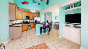 A kitchen with wooden cabinets, a microwave, and a refrigerator. There is a bar area with purple chairs and a television. - Ocean-view townhome with pool access, playground, outdoor shower - dog-friendly (Surf City)