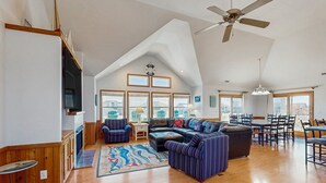 Ein geräumiges Wohnzimmer mit hoher Decke, einem großen Fenster, einem Deckenventilator und einem Essbereich mit Stühlen und Tisch.