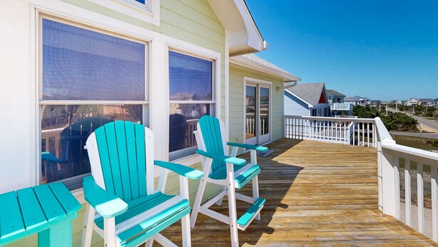 Eine Holzterrasse mit zwei türkisfarbenen Adirondack-Stühlen und einem weißen Geländer.