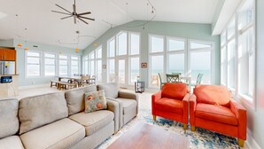 A spacious living room with a high ceiling, large windows, and a view of the beach. - Oceanfront Retreat with Premium Views, Roof Top Hot Tub, Private Pool, Game Room and More...! (Surf City)