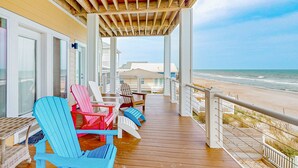 A wooden deck with colorful Adirondack chairs, a wicker table, and a view of the beach and ocean. - Oceanfront Retreat with Premium Views, Roof Top Hot Tub, Private Pool, Game Room and More...! (Surf City)