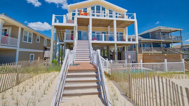 A beachfront hotel with multiple balconies, a central staircase, and a sandy beach area. - Oceanfront Retreat with Premium Views, Roof Top Hot Tub, Private Pool, Game Room and More...! (Surf City)