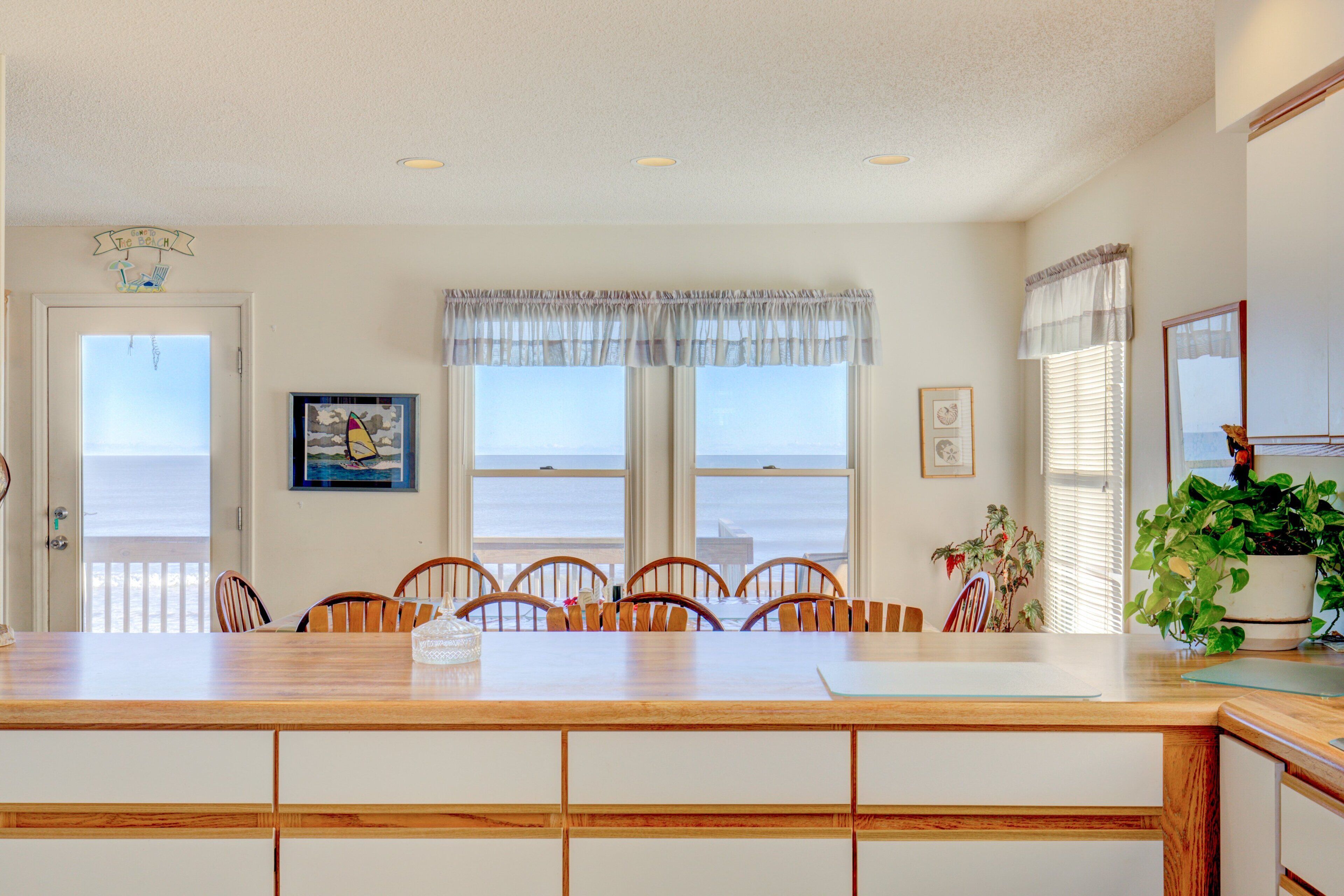 A dining area with a wooden table and chairs, a view of the ocean through large windows, and a ceiling fan.