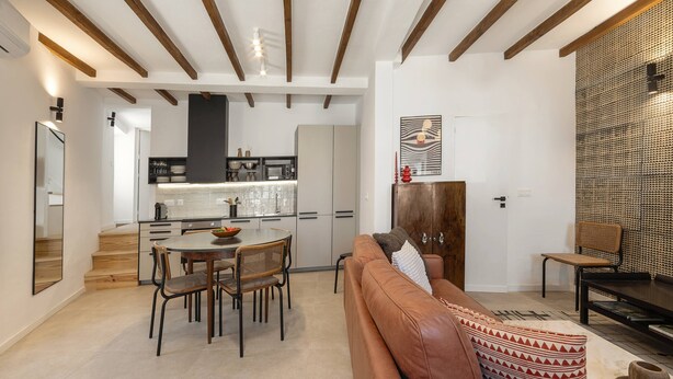 A modern kitchen with wooden beams, a dining area with a brown leather sofa, and a patterned wall.