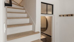 A staircase with wooden steps and a handrail, leading to a room with a mirror and a tiled wall.