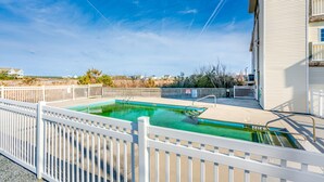 A swimming pool with a white fence, a building with a balcony, and a clear blue sky. - Studio condo with ocean views, pool, deck, & central AC (Surf City)