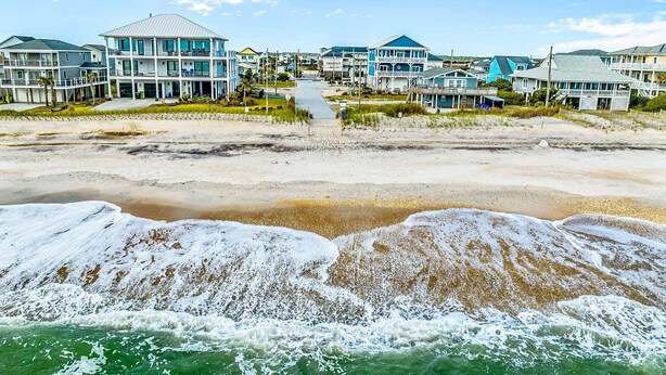 A beachfront property with multiple buildings, a sandy beach, and waves crashing onto the shore. - Studio condo with ocean views, pool, deck, & central AC (Surf City)