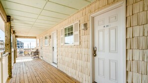A wooden deck with a covered area, white doors, and a view of a building in the background. - Studio condo with ocean views, pool, deck, & central AC (Surf City)
