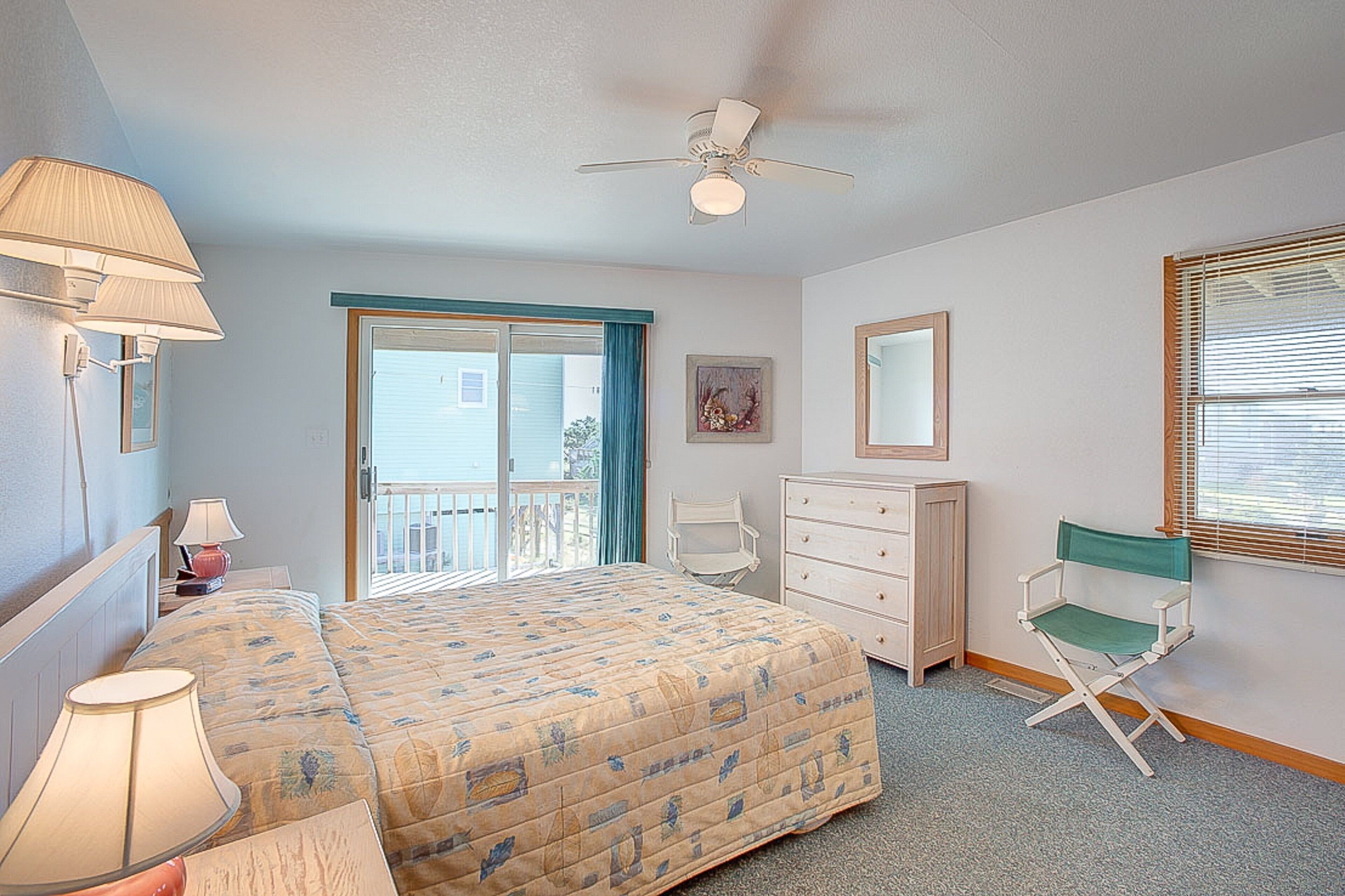 A bedroom with a bed, dresser, chair, lamp, ceiling fan, and a view through a window.
