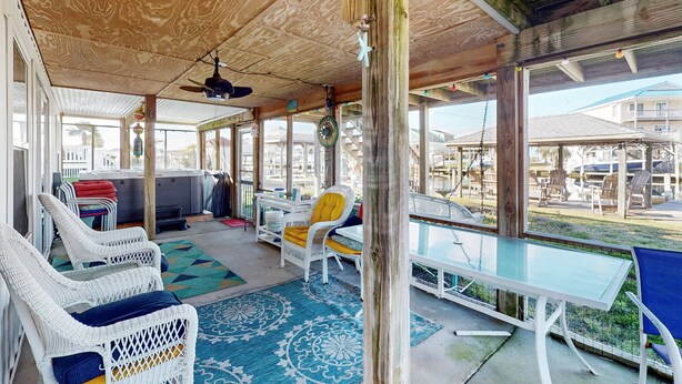 A covered outdoor seating area with wicker chairs, a glass table, and a view of the surrounding buildings. - Dog-friendly Sound Front Duplex with Screened-in patio, hot tub and dock (Surf City)
