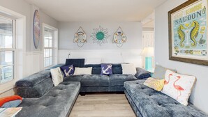 A living room with a grey sectional sofa, decorative wall art, and a framed poster. - Dog-friendly Sound Front Duplex with Screened-in patio, hot tub and dock (Surf City)