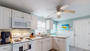 A kitchen with white cabinets, a microwave, stove, and a ceiling fan. - Dog-friendly Sound Front Duplex with Screened-in patio, hot tub and dock (Surf City)