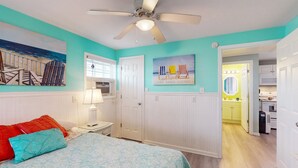 A bedroom with a bed, a ceiling fan, a window, and a door leading to a kitchen. - Dog-friendly Sound Front Duplex with Screened-in patio, hot tub and dock (Surf City)