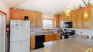 A kitchen with wooden cabinets, a white refrigerator, a black dishwasher, a microwave, a stove, and a granite countertop. - SEMI-OCEANFRONT-5 BR, 3 Full & 1 Half Bath-just two lots from the beach walkway (Avon)
