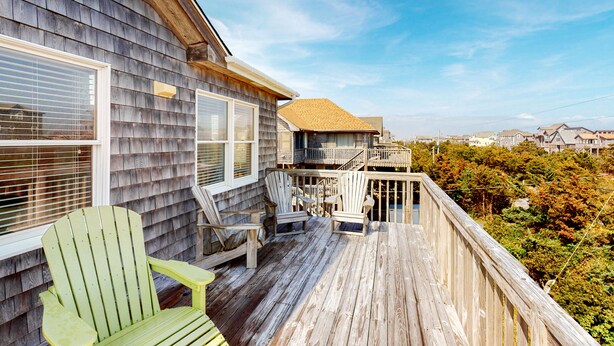 A wooden deck with Adirondack chairs, a small table, and a view of the surrounding area. - SEMI-OCEANFRONT-5 BR, 3 Full & 1 Half Bath-just two lots from the beach walkway (Avon)