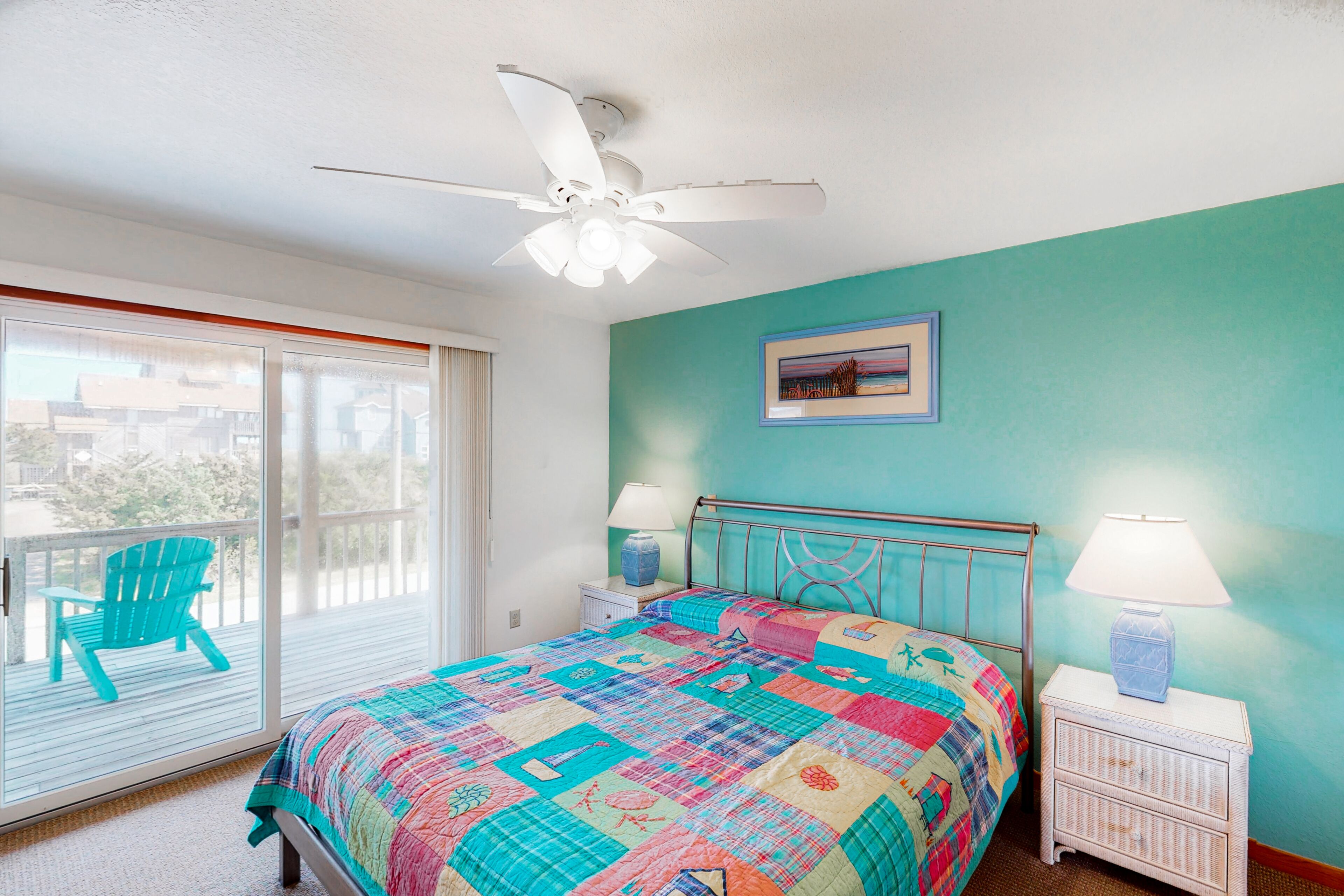 A bedroom with a bed, a ceiling fan, a window with a view, and a chair outside.