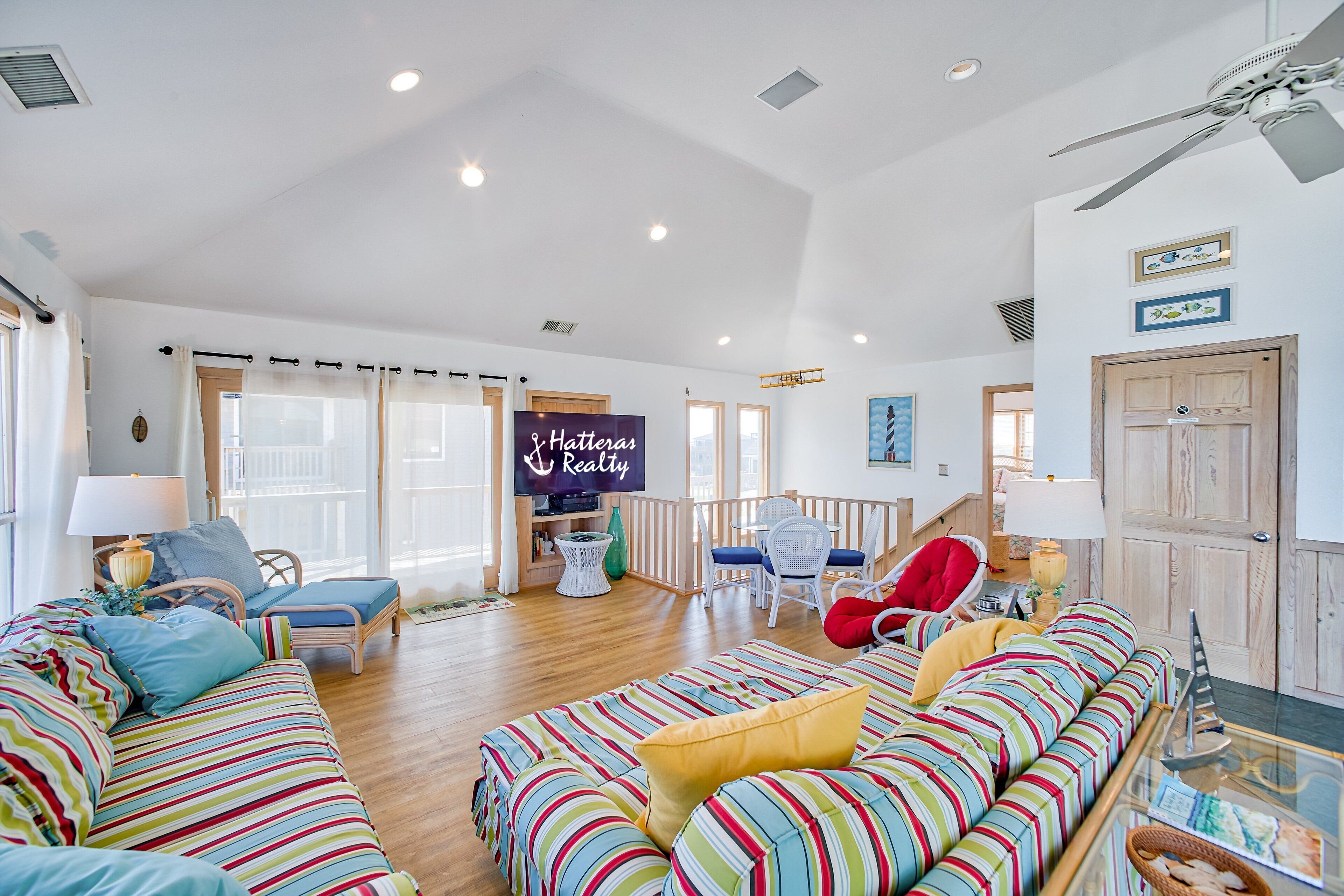 Ein geräumiges Wohnzimmer mit einer großen Couch, einem Essbereich und einem Fernseher, der 'Hatteras Realty' zeigt.